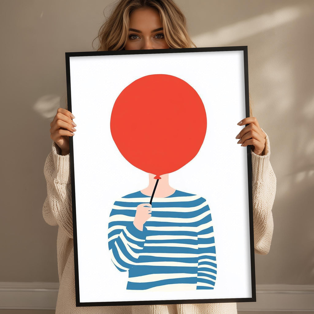 A woman holding a framed print of a red balloon with a face on it.