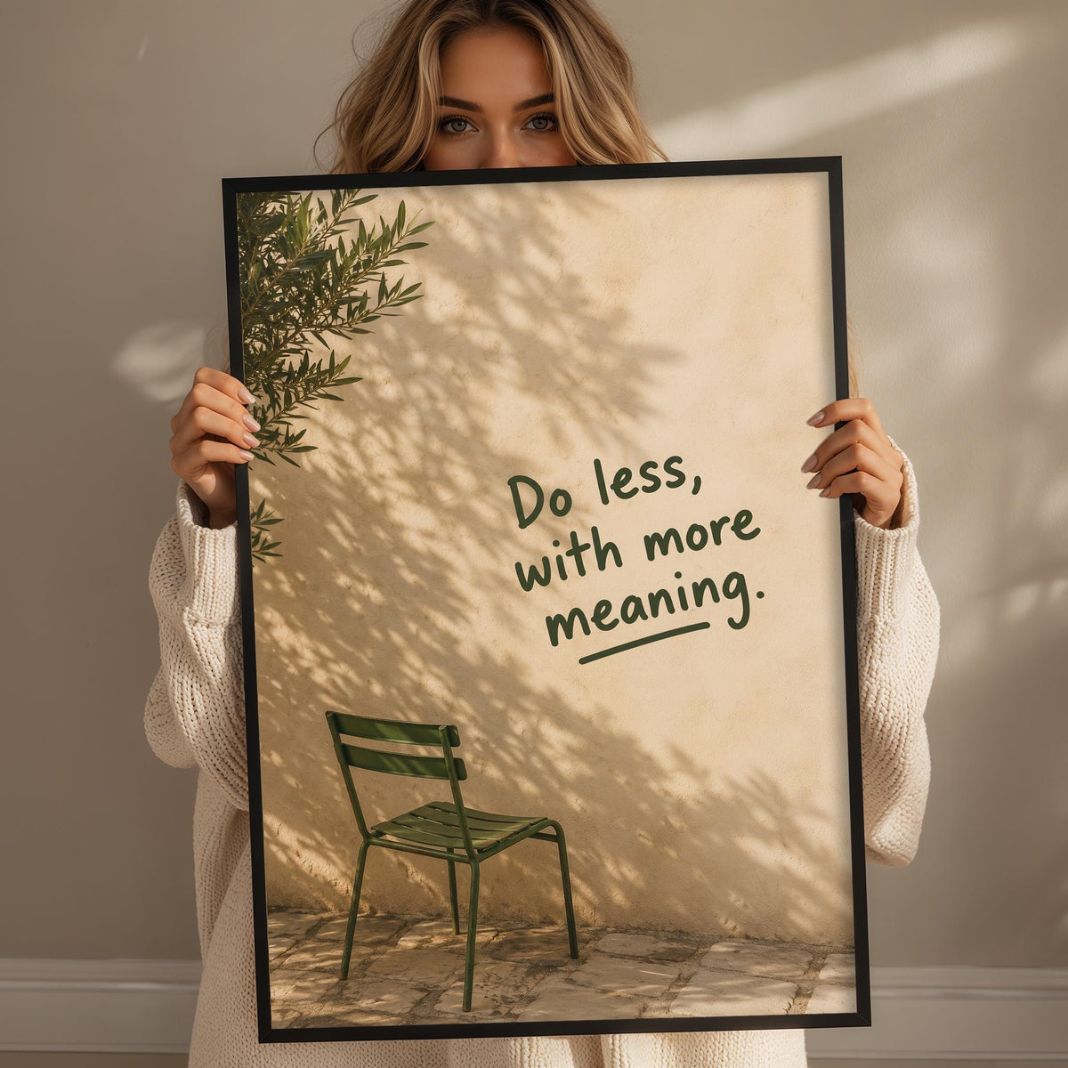 A woman holding a framed poster with a green chair and a tree in the background.