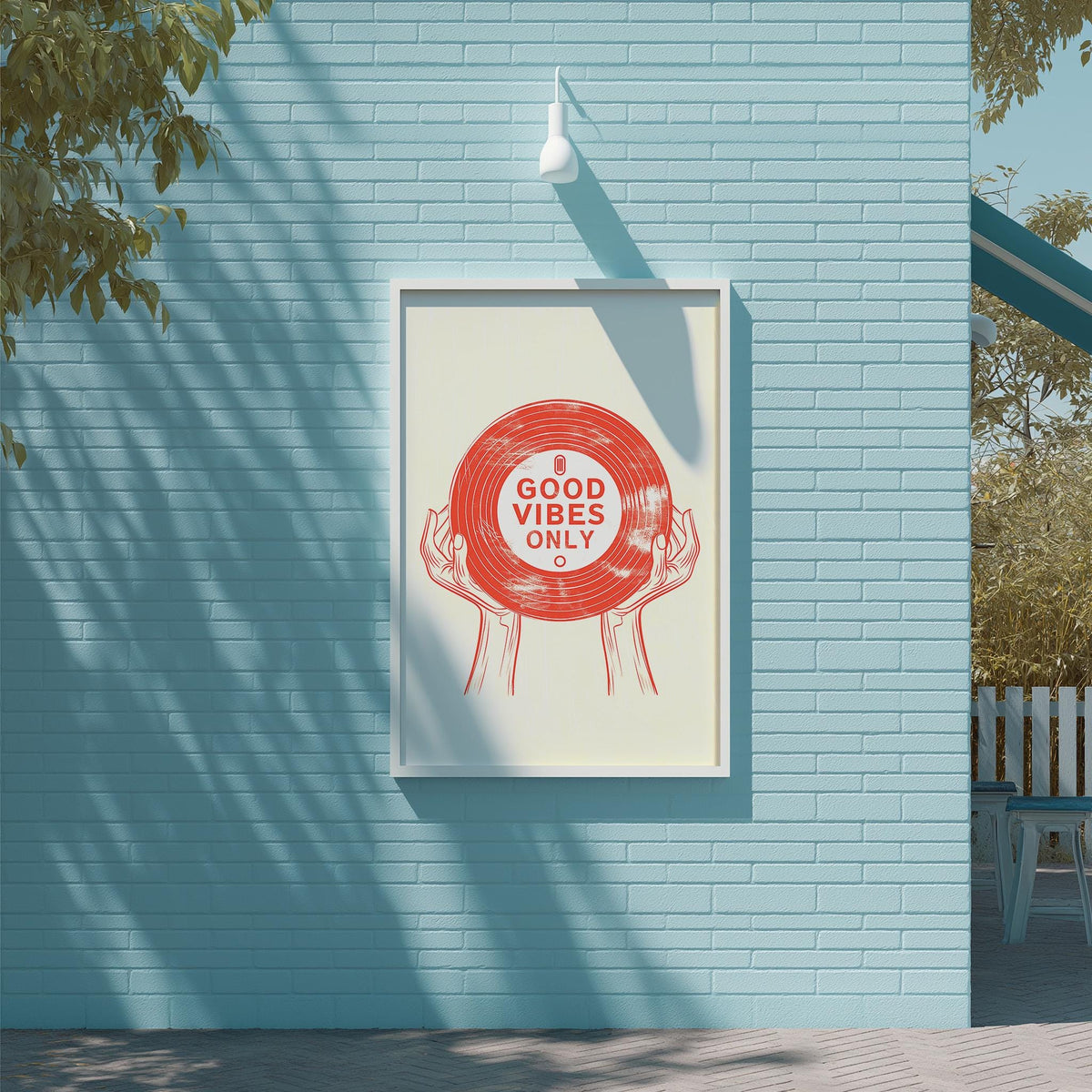 A framed poster with the text "GOOD VIBES ONLY" is displayed on a blue brick wall, with a white light fixture above it.