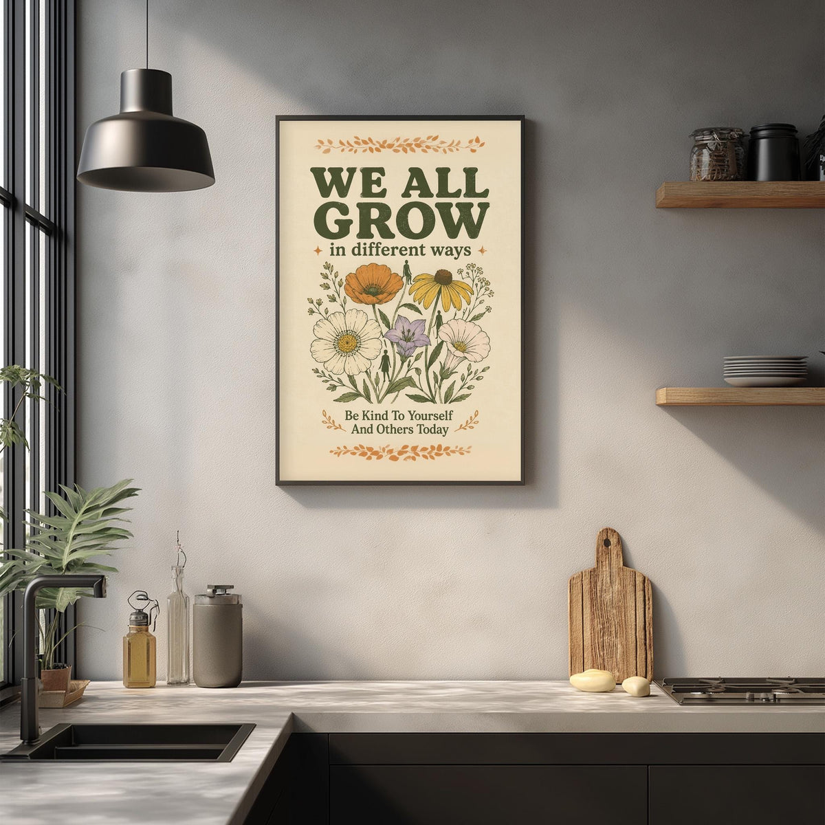 a framed poster with the text "WE ALL GROW in different ways" and an illustration of flowers, hanging on a wall above a kitchen counter with various kitchen items such as a cutting board, a soap dispenser, and a plant.