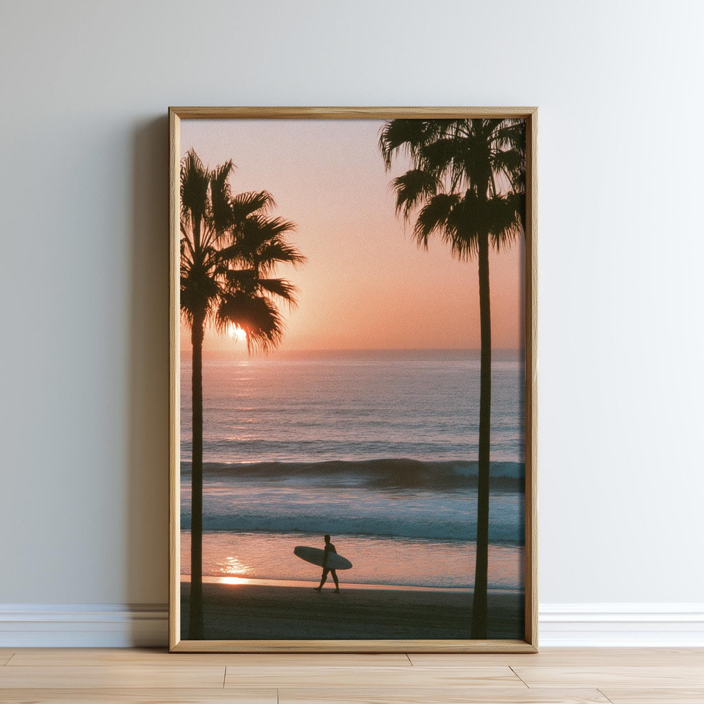 A framed photograph depicting a surfer walking along a beach at sunset, with palm trees in the foreground.
