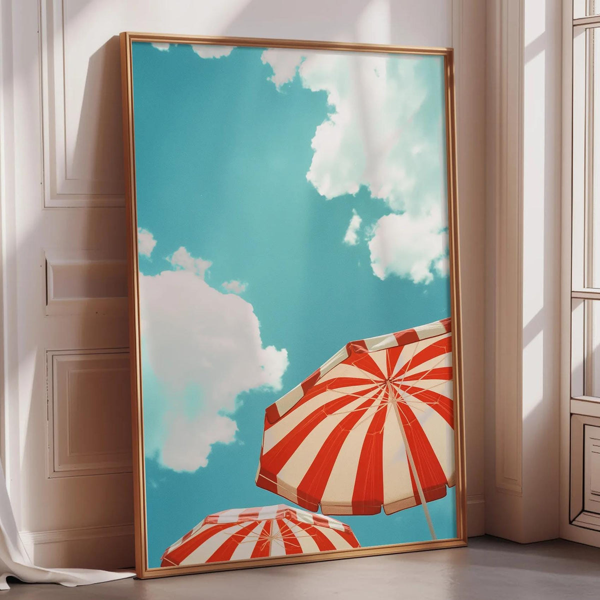 A large framed print depicting a bright blue sky with fluffy white clouds and two red and white striped umbrellas.