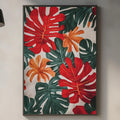 a kitchen counter with a framed print of tropical leaves hanging on the wall above it. The print has a vibrant mix of red, orange, and green leaves, creating a lively and colorful atmosphere in the kitchen.