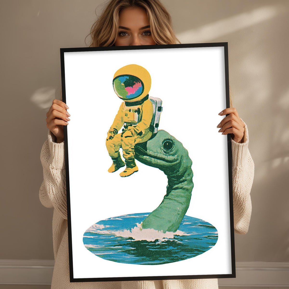 A woman holds a framed artwork depicting an astronaut in a yellow suit sitting on a green sea turtle.
