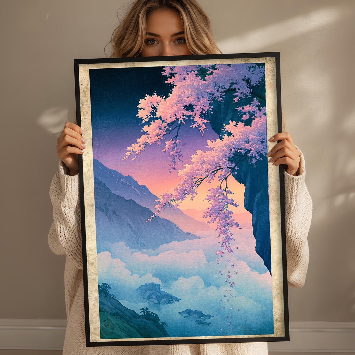 A woman holds up a framed painting depicting a serene landscape with mountains, clouds, and cherry blossoms.