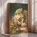 A framed painting depicting a green frog perched on a skull surrounded by mushrooms and plants, set against a dark background.