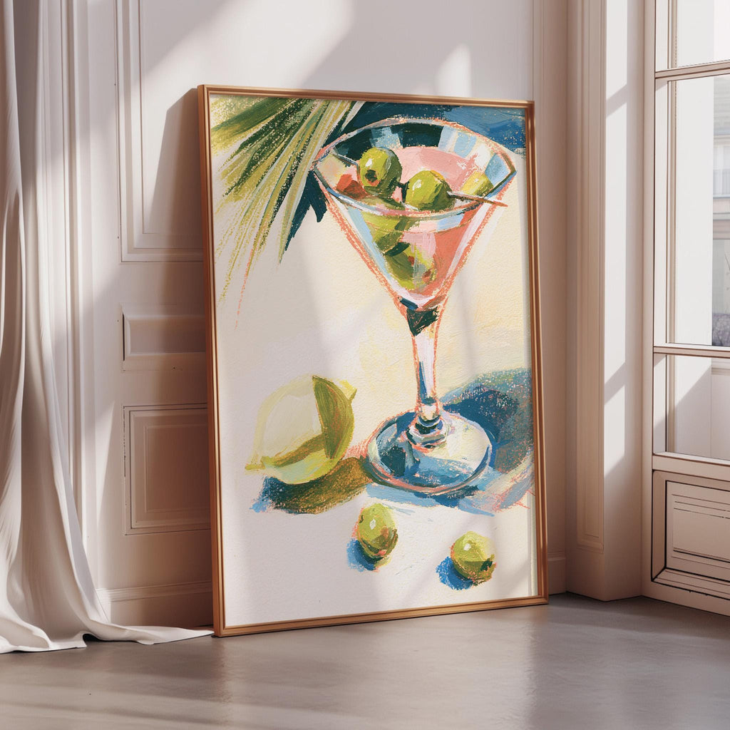 a framed painting of a martini glass filled with olives, placed on a white wall near a window.