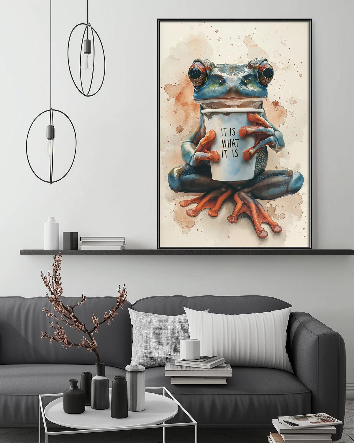 a large framed painting of a frog sitting on a coffee cup, with the text "IT IS WHAT IT IS" written on the cup. The painting is displayed above a gray couch in a living room setting.