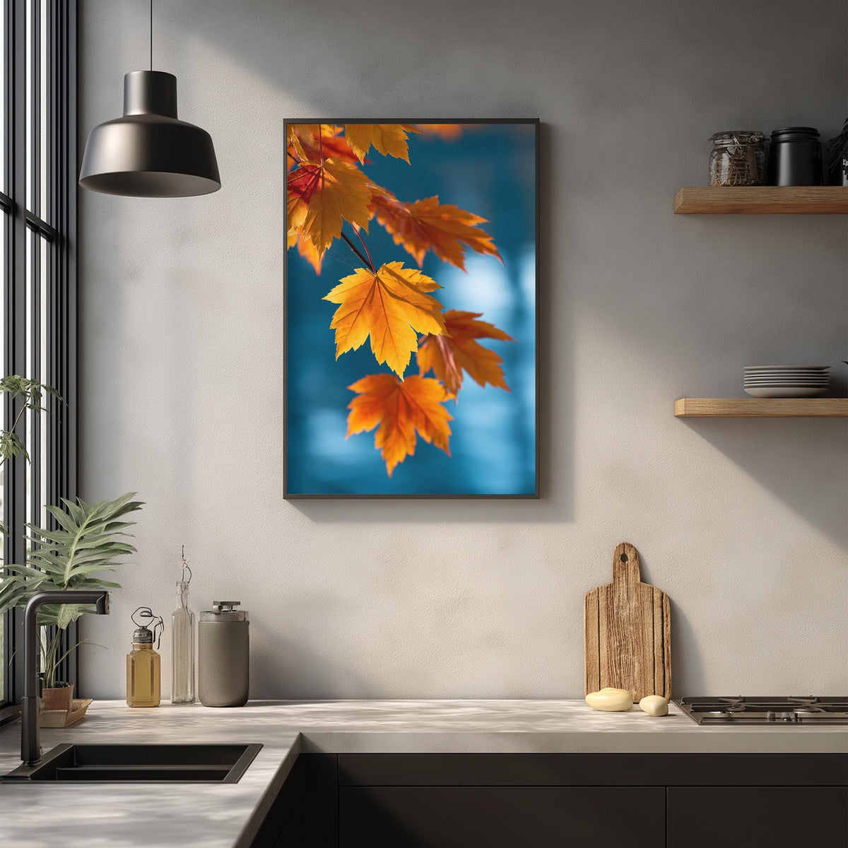 a kitchen counter with a framed picture of orange and yellow autumn leaves hanging above it. The counter has various kitchen items, such as a cutting board, a soap dispenser, and a bottle. The overall scene has a warm and cozy atmosphere, with the natural colors of the leaves contrasting against the neutral tones of the kitchen.