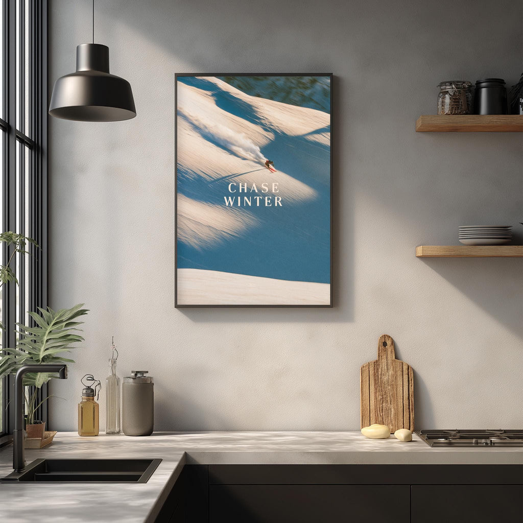 a kitchen counter with various kitchen items, such as a cutting board, a bottle, and a bowl, as well as a framed poster of a person skiing on a snowy mountain.