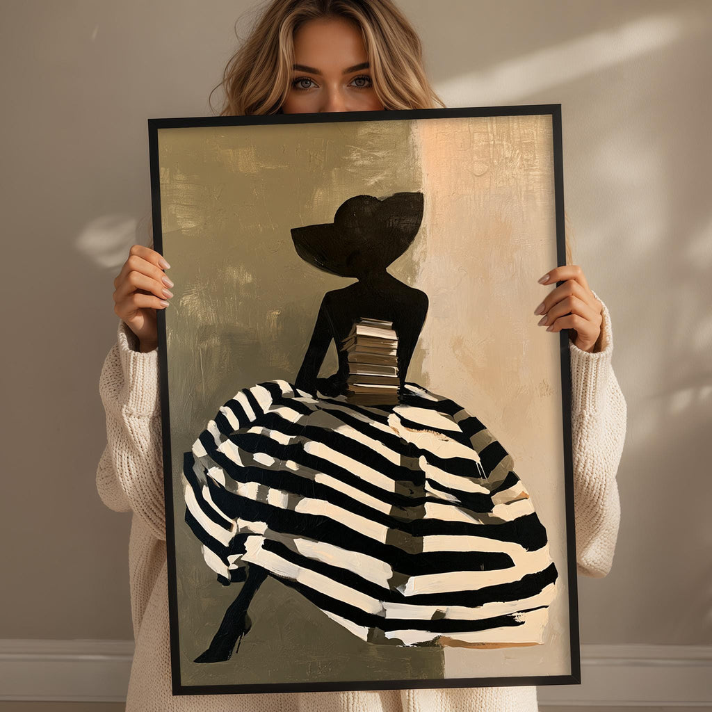 A woman holding a framed painting of a woman in a dress with a large hat, standing in front of a wall.