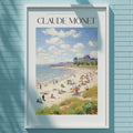 A framed painting of a beach scene hangs on a light blue wall, with a white light fixture above it.
