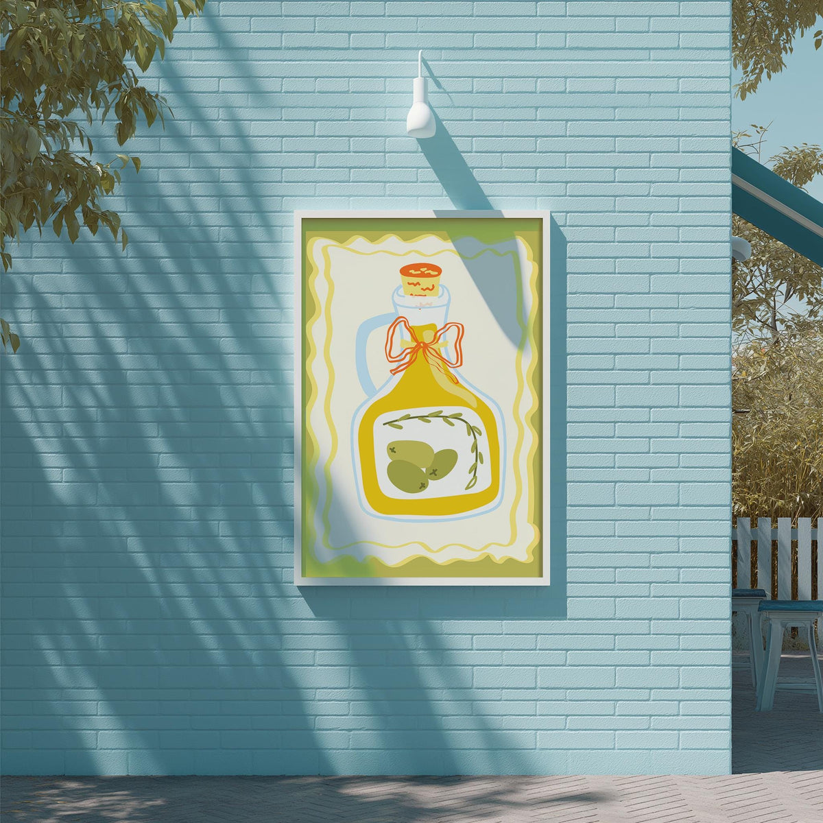 A framed illustration of a bottle of olive oil is displayed on a blue brick wall, with a white light fixture above it.