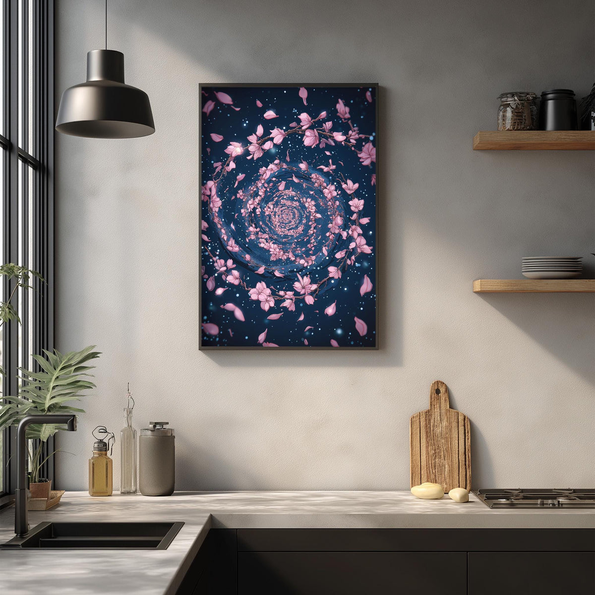 a kitchen counter with a framed artwork of pink flowers and a wooden cutting board on it. The kitchen has a modern design with a black countertop, a hanging light fixture, and various kitchen items such as a sink, a bottle, and a bowl.