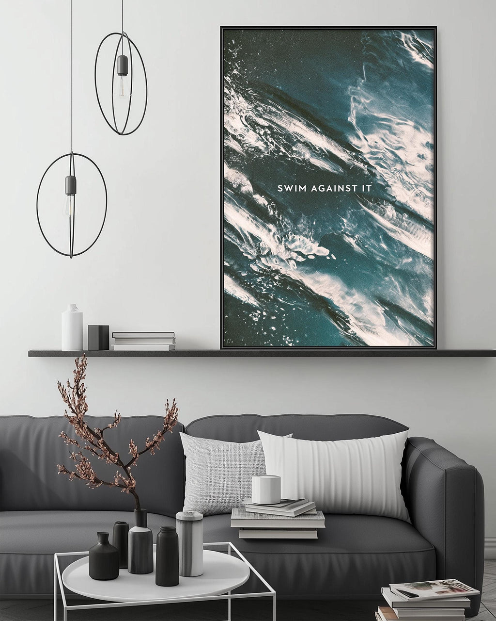 a modern living room with a gray sofa, a coffee table, and a large framed poster of ocean waves above it. The poster has the text "SWIM AGAINST IT" written on it.