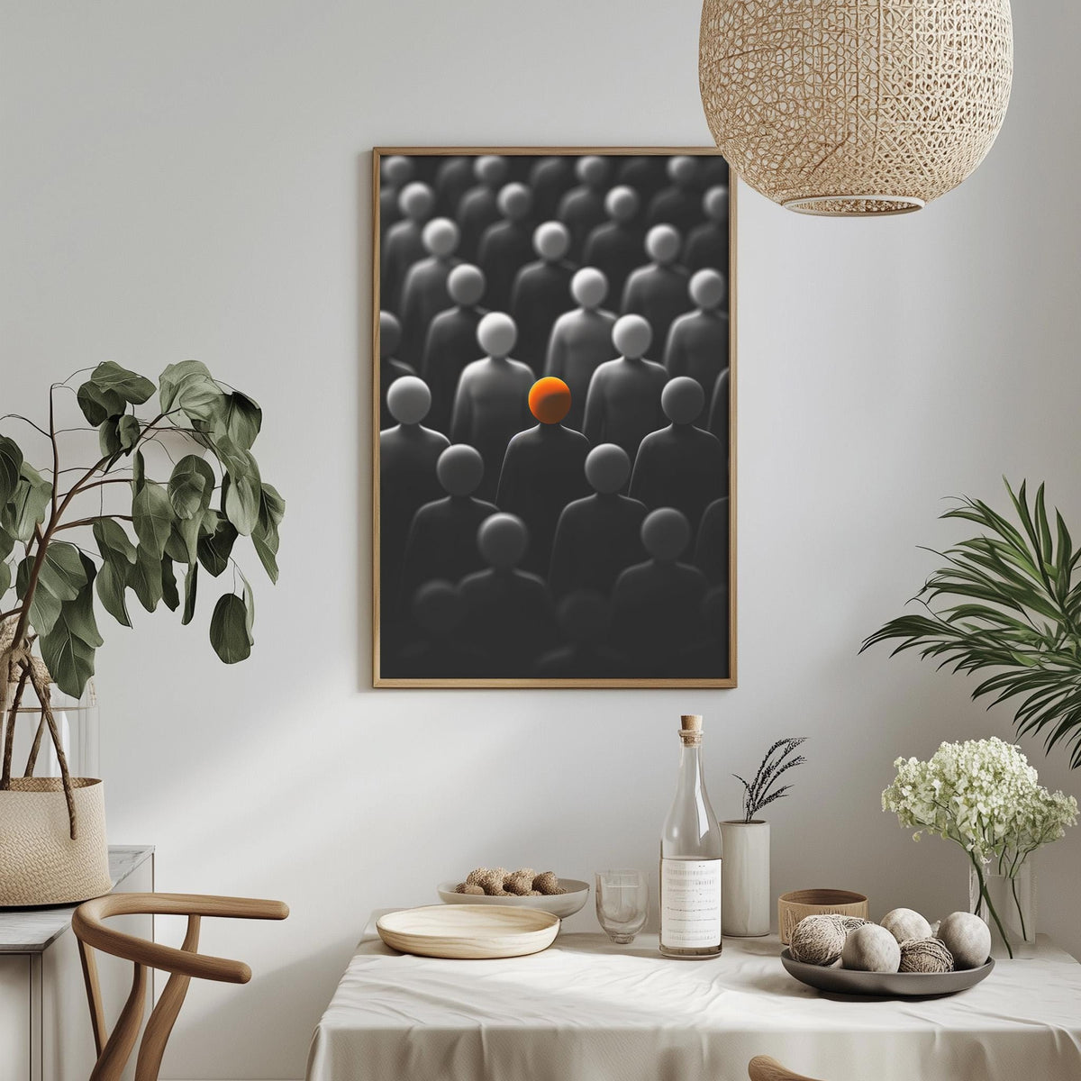 a dining table with a white tablecloth, a bowl of fruit, a bottle, and a vase with flowers. Above the table, there is a framed picture of a group of people with an orange object in the center.