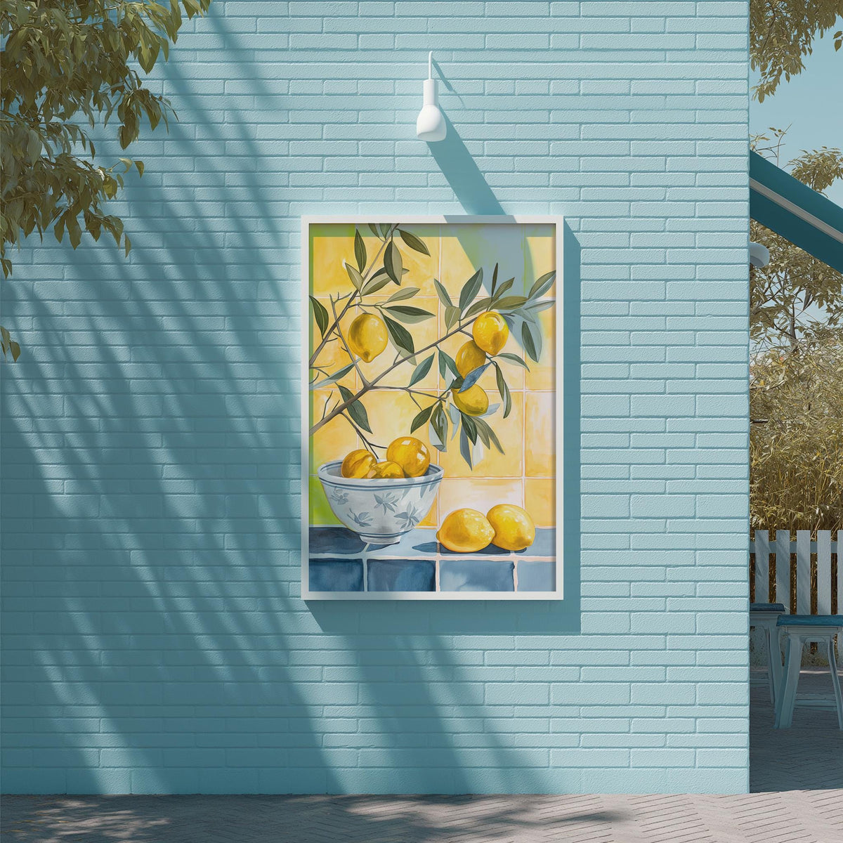 A framed painting of a bowl of lemons is displayed on a blue brick wall, with a tree and a white light fixture above it.