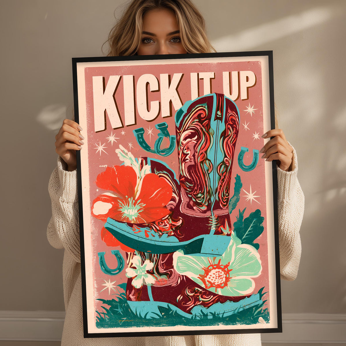 A woman holding a framed poster with a colorful illustration of a cowboy boot and flowers.