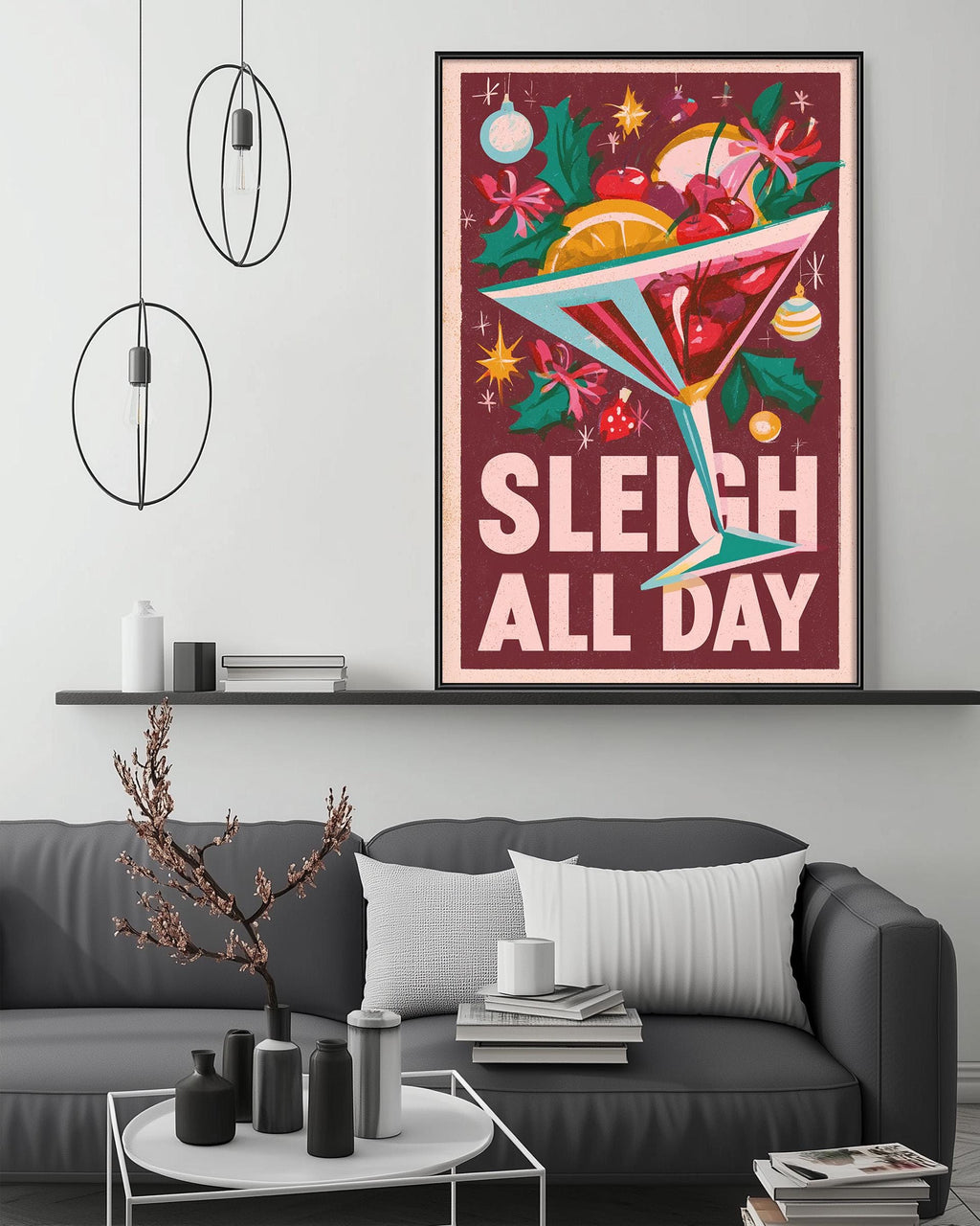 a cozy living room with a gray couch, a coffee table, and a framed poster on the wall. The poster has a festive design with a martini glass filled with colorful fruit and a "Sleigh All Day" message.