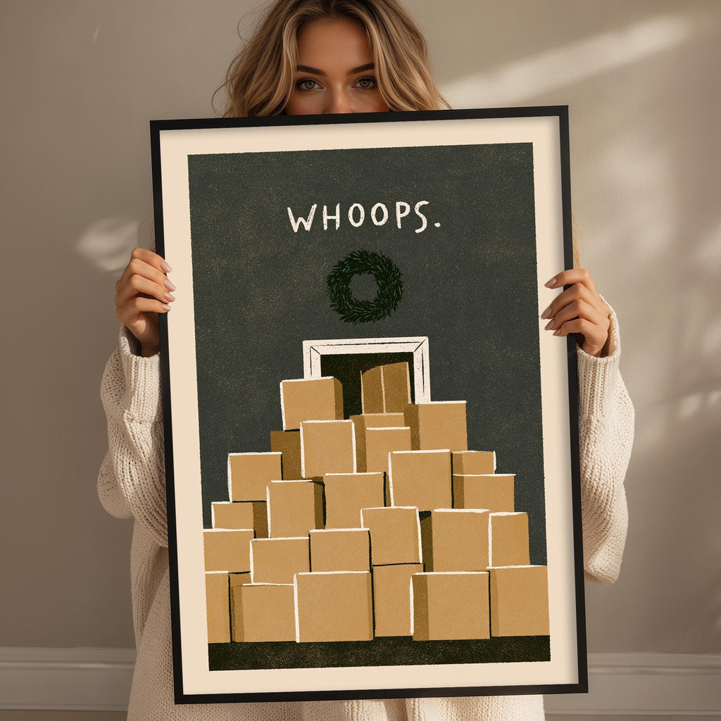 A woman holding a framed print with a wreath and a stack of brown boxes.