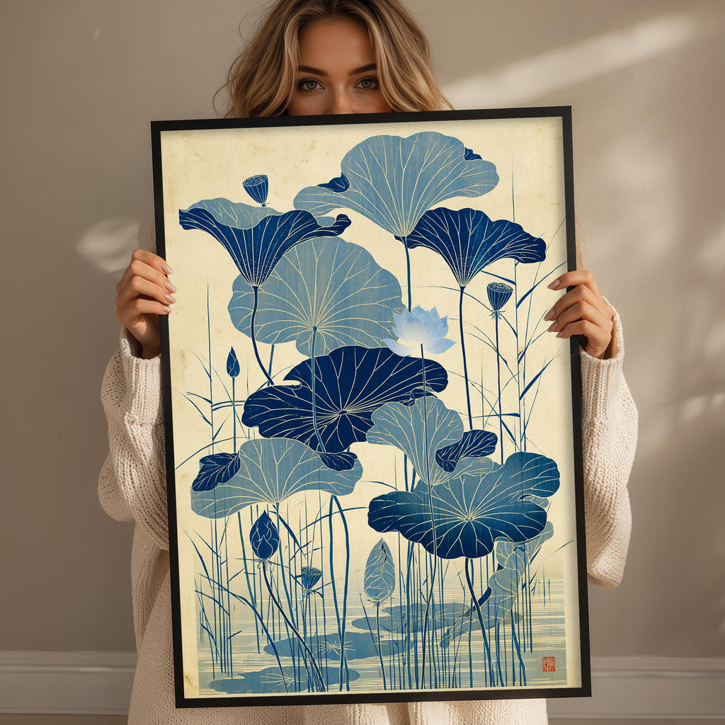 A woman is holding up a framed print with a blue and white floral design depicting lotus flowers.