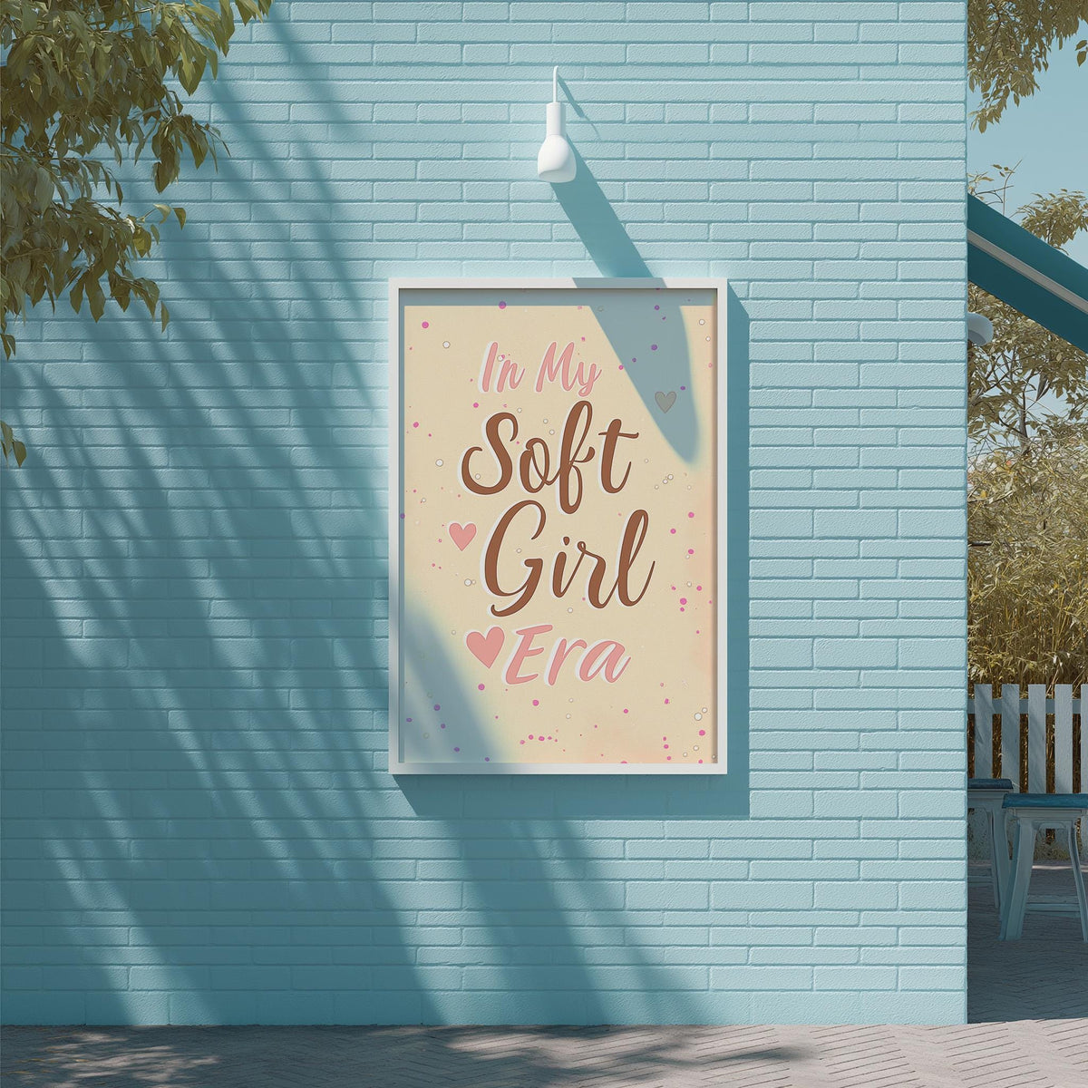 A framed poster with the text "In My Soft Girl Era" is displayed on a blue brick wall, with a tree and a white light fixture visible in the background.