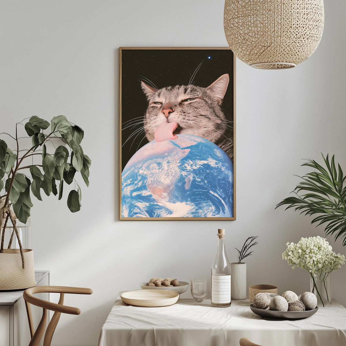 a framed picture of a cat licking a globe, which appears to be a representation of the Earth. The cat is positioned in the center of the frame, with the globe in the background. The scene is set against a white wall, with a potted plant and a vase of flowers visible on either side of the frame.