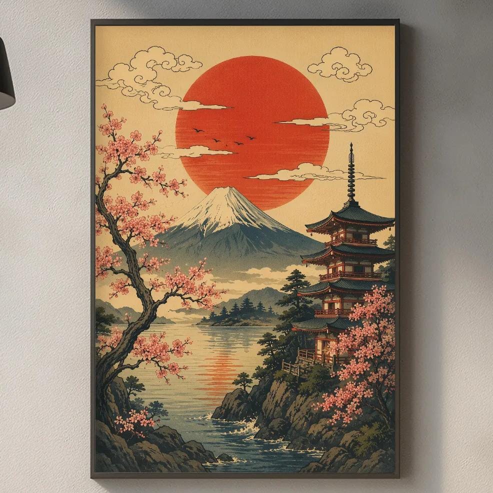 a kitchen counter with a framed Japanese landscape painting hanging above it. The painting depicts a serene scene of a mountain landscape with a temple, surrounded by cherry blossoms and a large sun in the sky. The kitchen counter has various items on it, including a cutting board, a bottle, and a vase.