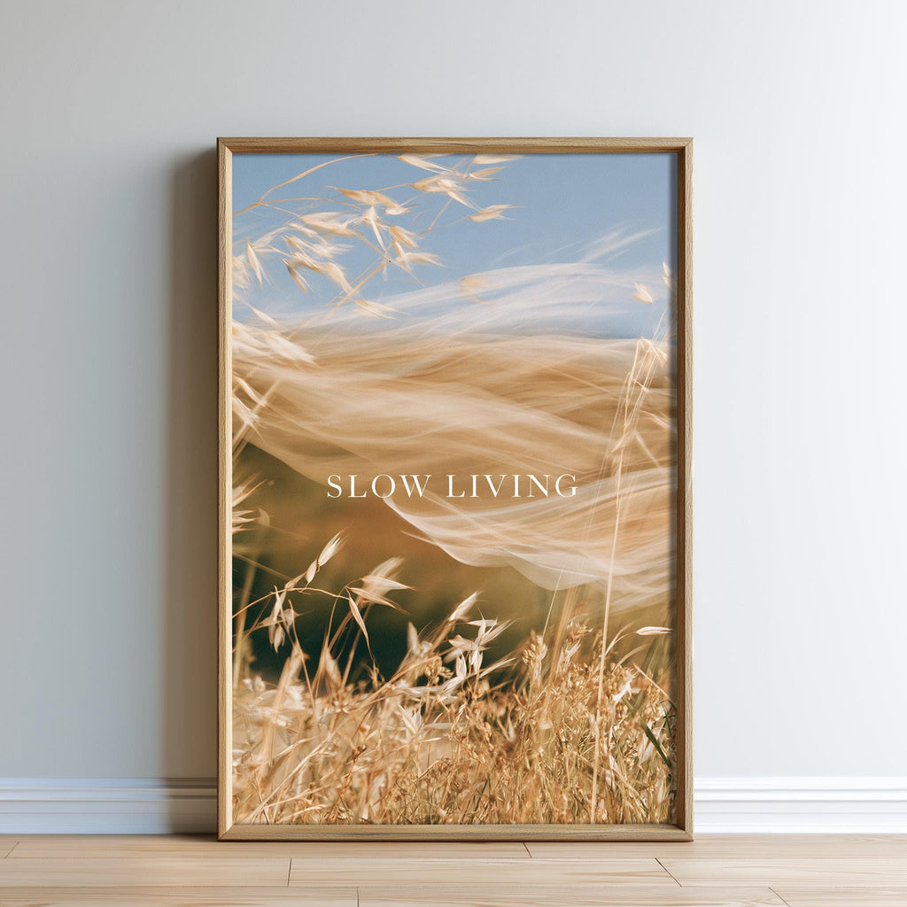 The image is a framed print of a blurred wheat field with the text "SLOW LIVING" displayed prominently in the center.