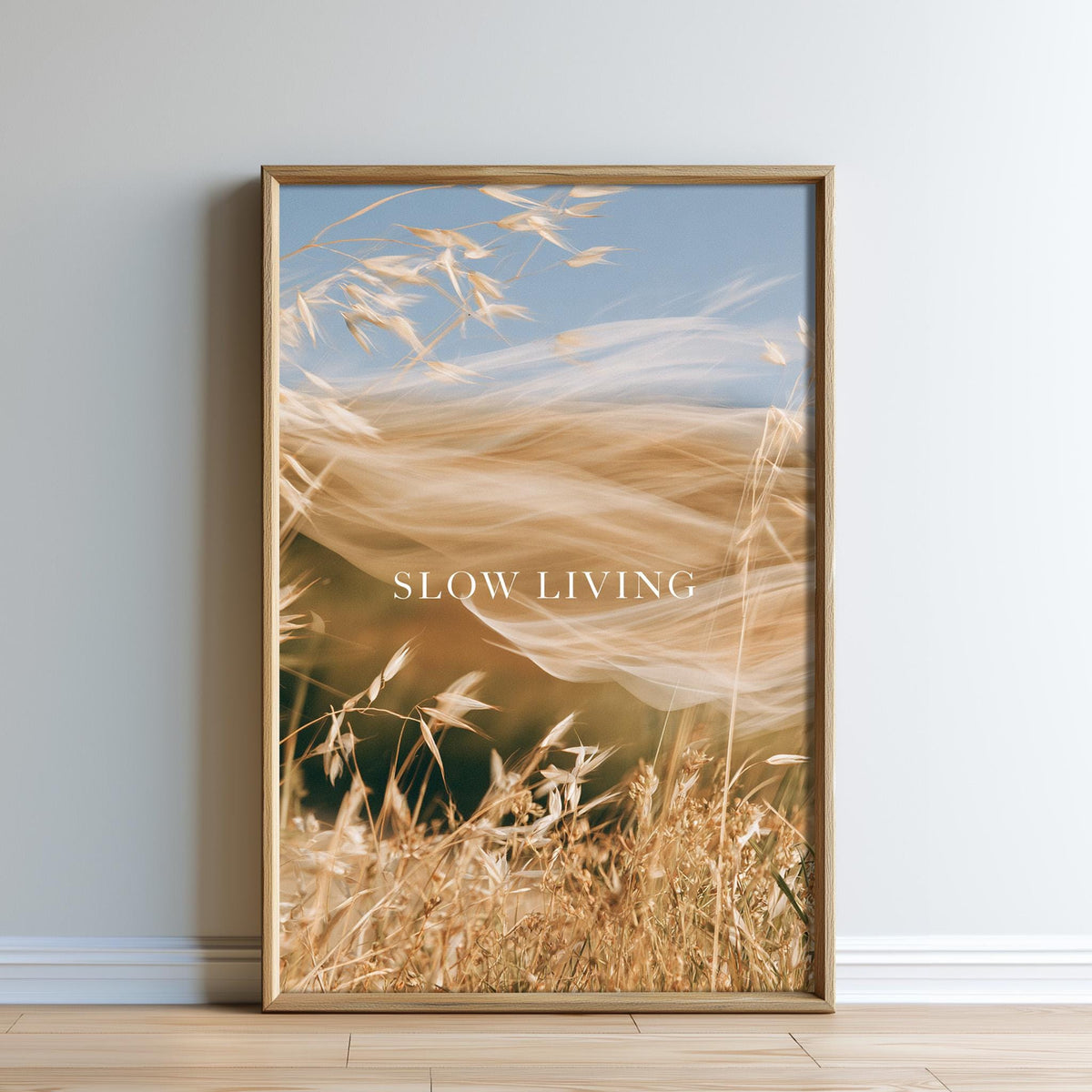 The image is a framed print of a blurred wheat field with the text "SLOW LIVING" displayed prominently in the center.