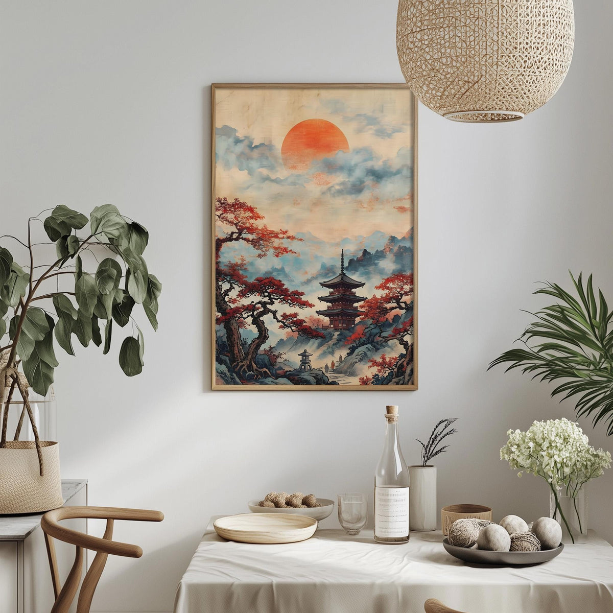 a serene indoor setting with a large framed painting of a Japanese temple set against a backdrop of a sunset over a mountainous landscape. The painting is hung on a white wall above a dining table, which is adorned with various decorative items such as potted plants, vases, and bowls. A bottle and a wine glass are also present on the table, suggesting a dining or relaxation area.