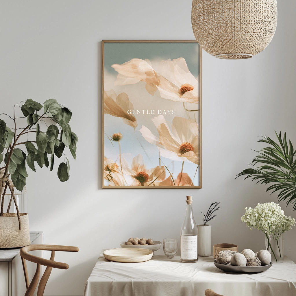 a dining table with a white tablecloth, a bowl of fruit, a bottle, and a vase with flowers. Above the table, there is a framed picture of flowers hanging on the wall.
