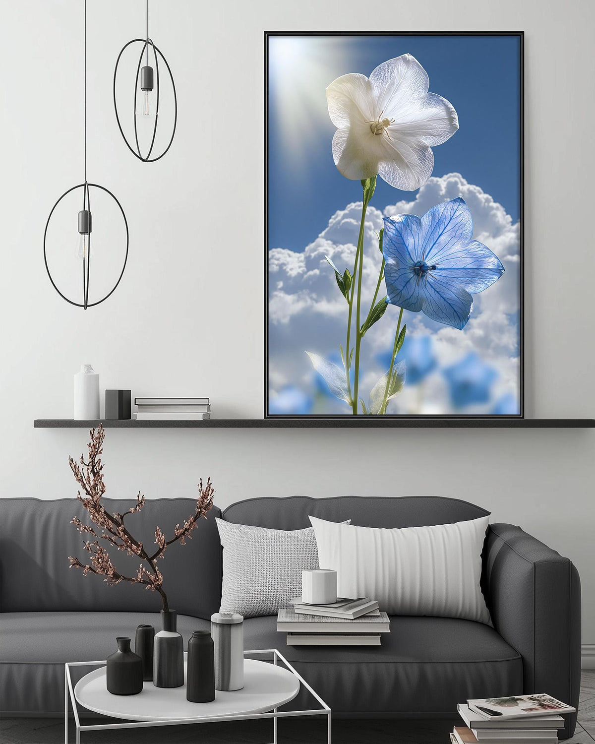 a large framed picture of two flowers, one white and one blue, set against a backdrop of a blue sky with fluffy white clouds. The picture is hanging on a wall above a gray couch, which is adorned with various decorative items such as a potted plant, vases, and books. The overall setting appears to be a cozy and inviting living space.