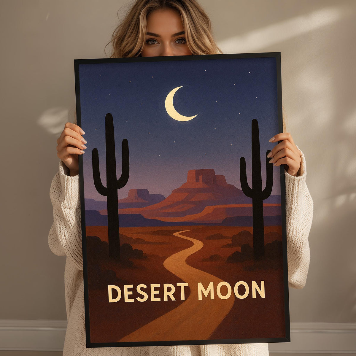 A woman holds up a framed poster depicting a desert landscape with cacti and a crescent moon in the night sky.