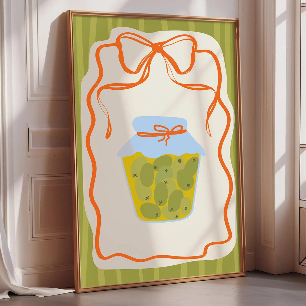 A framed illustration of a jar of pickles with a bow on top, placed on a wooden floor next to a window.