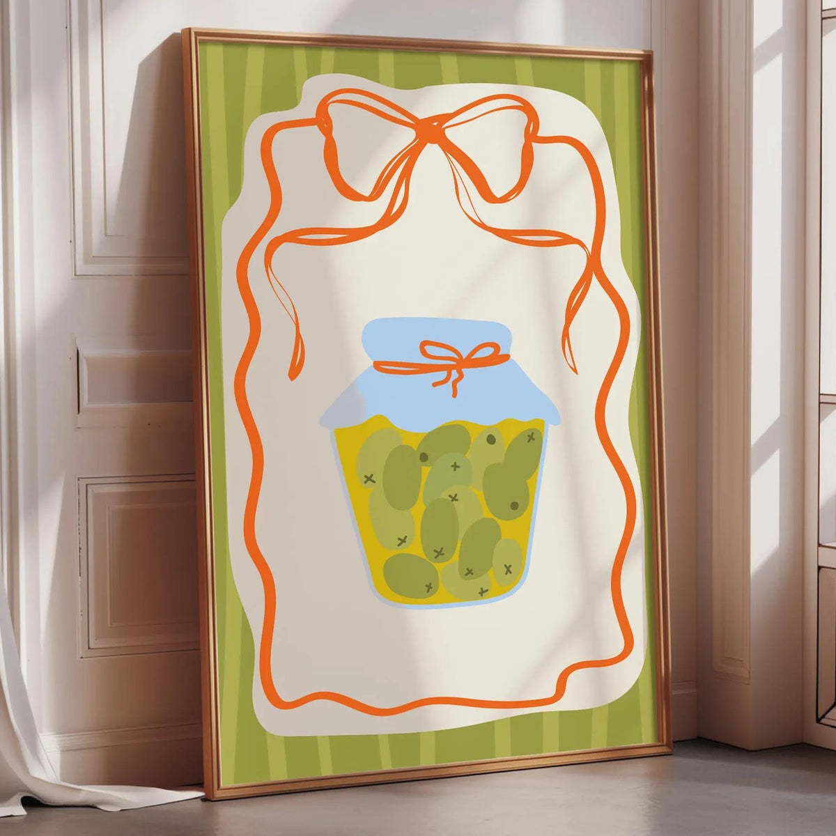 A framed illustration of a jar of pickles with a bow on top, placed on a wooden floor next to a window.