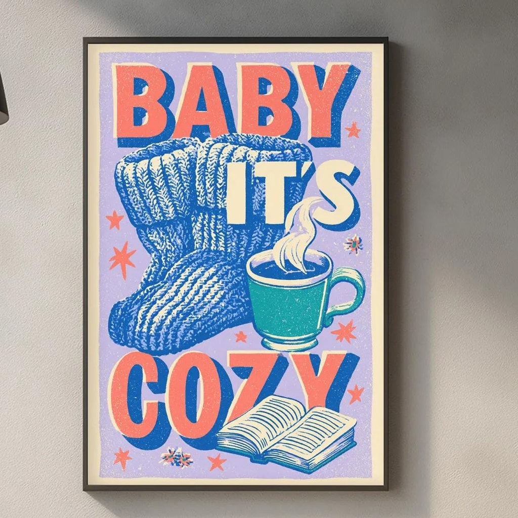 a kitchen counter with various items, including a framed poster with the text "BABY IT'S COZY" and illustrations of a pair of mittens and a cup of hot chocolate.