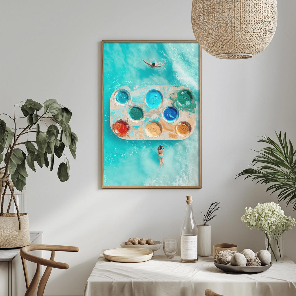 a dining table with a white tablecloth, a bowl of fruit, a bottle, and a vase with flowers. Above the table, there is a framed picture of a person swimming in a pool with a palette of colors.
