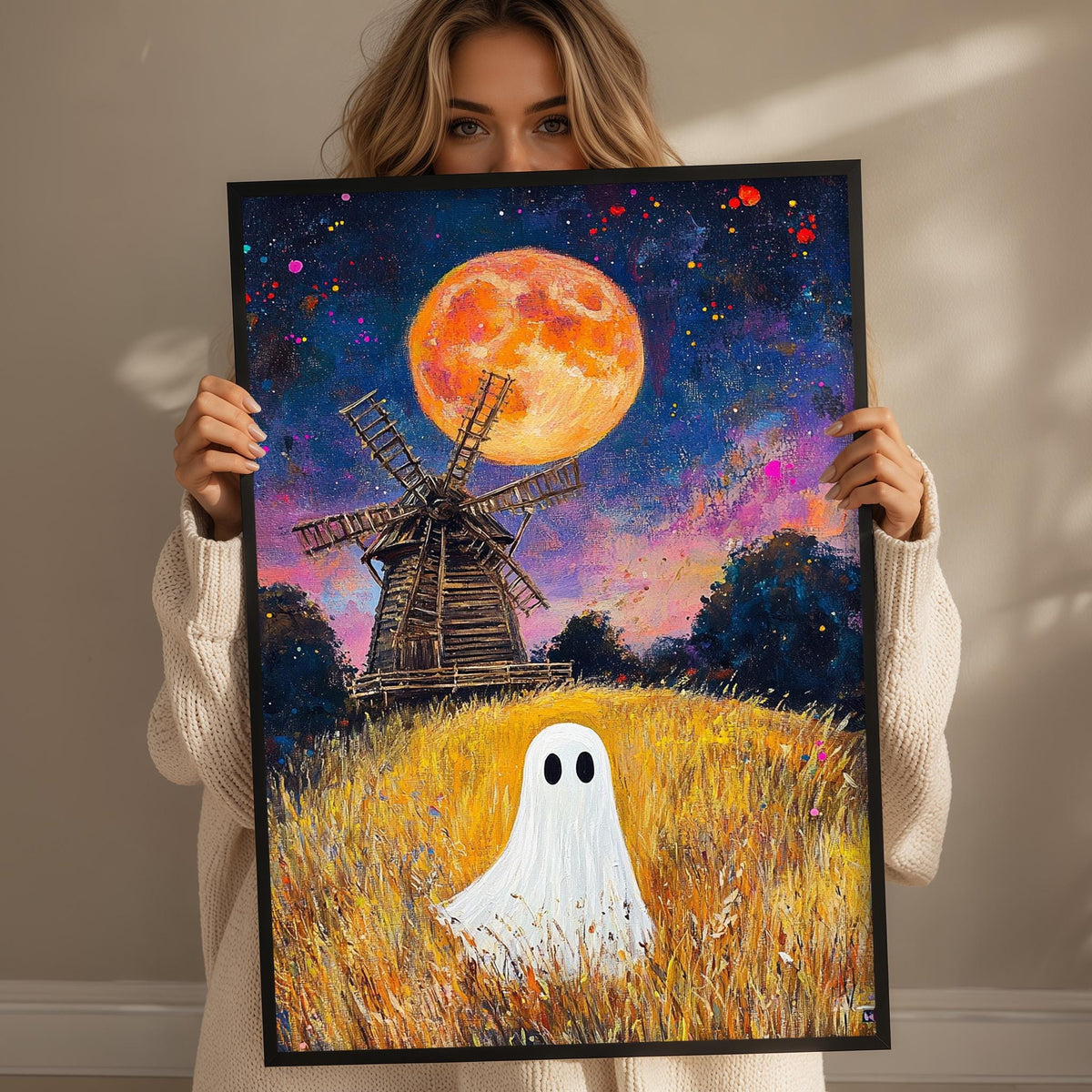 A woman holds up a framed painting depicting a ghost in a field with a windmill in the background, under a large orange moon.