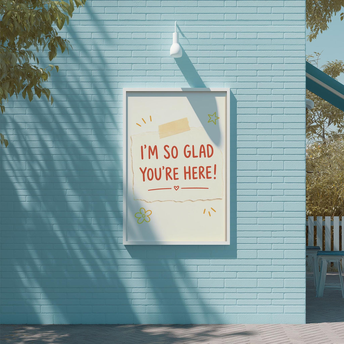 A framed poster with the text "I'm so Glad You're Here!" displayed on a blue brick wall.