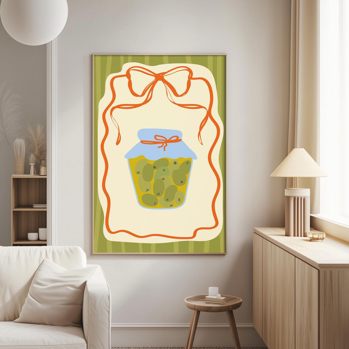 a cozy living room with a white sofa, a wooden side table, and a lamp. A large framed picture of a jar of pickles is hanging on the wall, with a red ribbon around it.