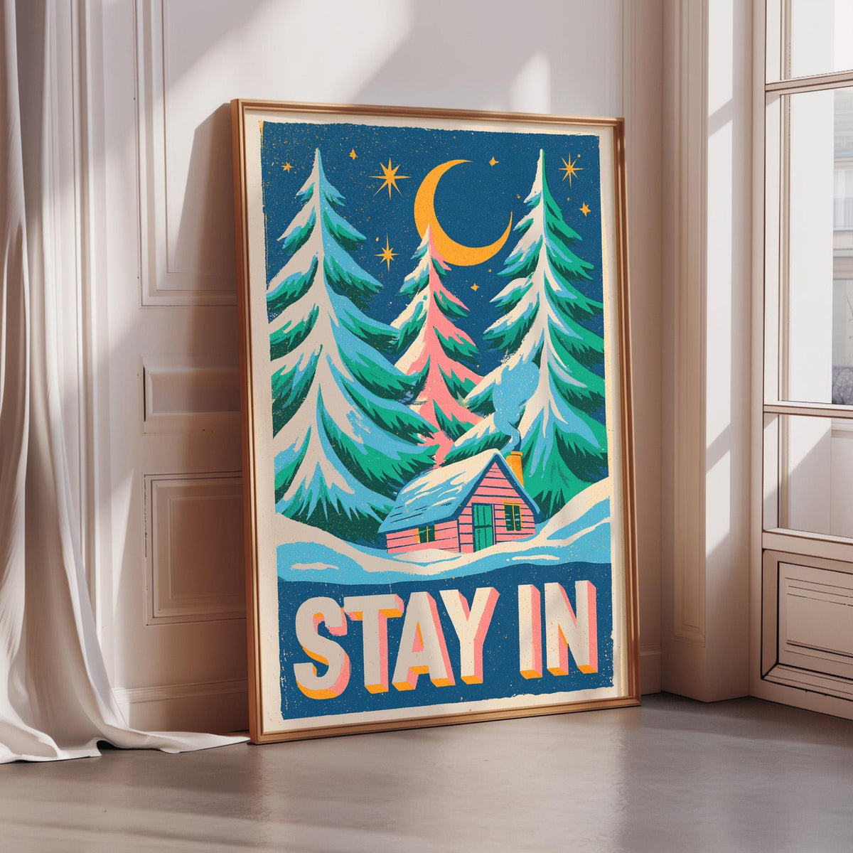 A framed poster with a winter scene depicting a snowy landscape with pine trees, a cabin, and a crescent moon in the night sky. The poster has the text "STAY IN" written on it.