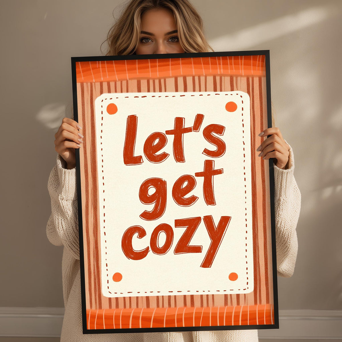 A woman holding a framed sign with the text "Let's get cozy" written on it.