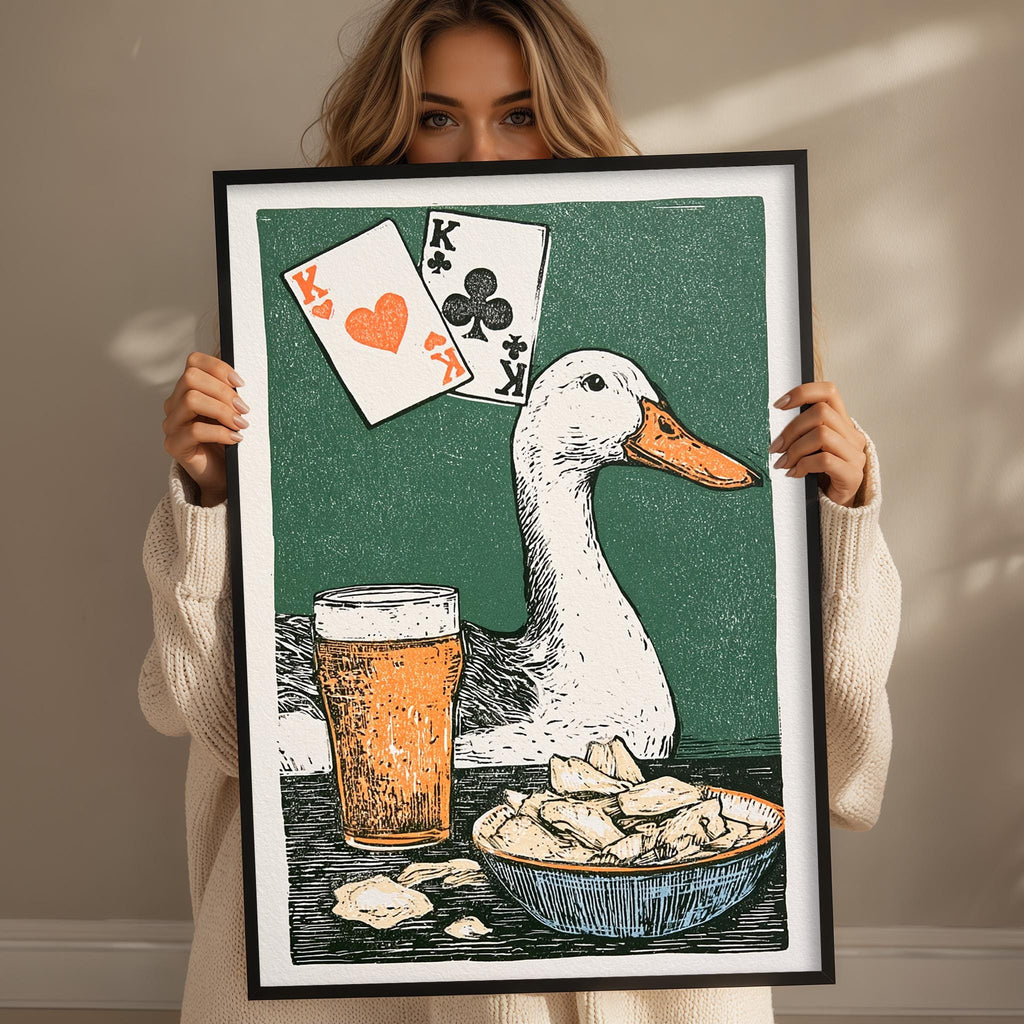 A woman holds up a framed illustration depicting a white duck with a heart-shaped face, a deck of playing cards, a glass of beer, and a bowl of chips.