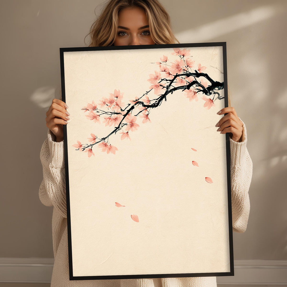 A woman holding a framed print of a cherry blossom branch with pink flowers.