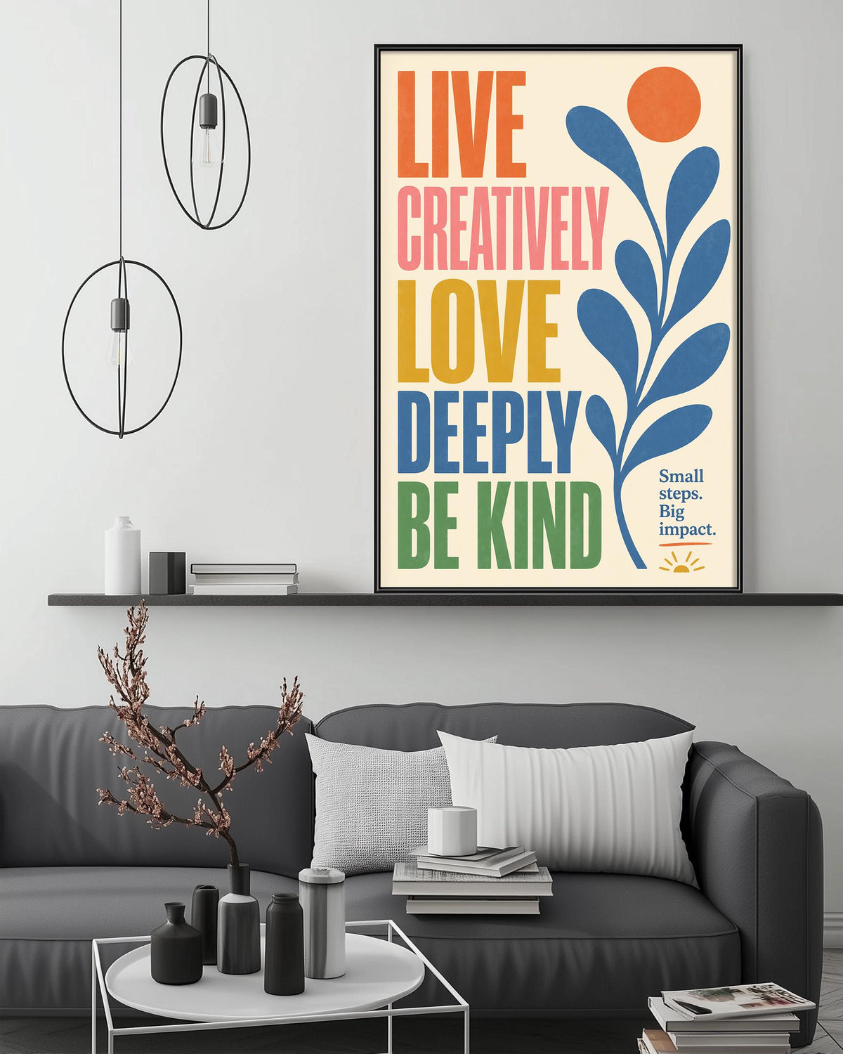 a poster with the text "Live Creatively, Love Deeply, Be Kind" displayed on a wall above a gray couch with a coffee table in front of it.