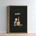 A framed poster with a skeleton sitting next to a lit candle, with the word "COZY" written above the image.