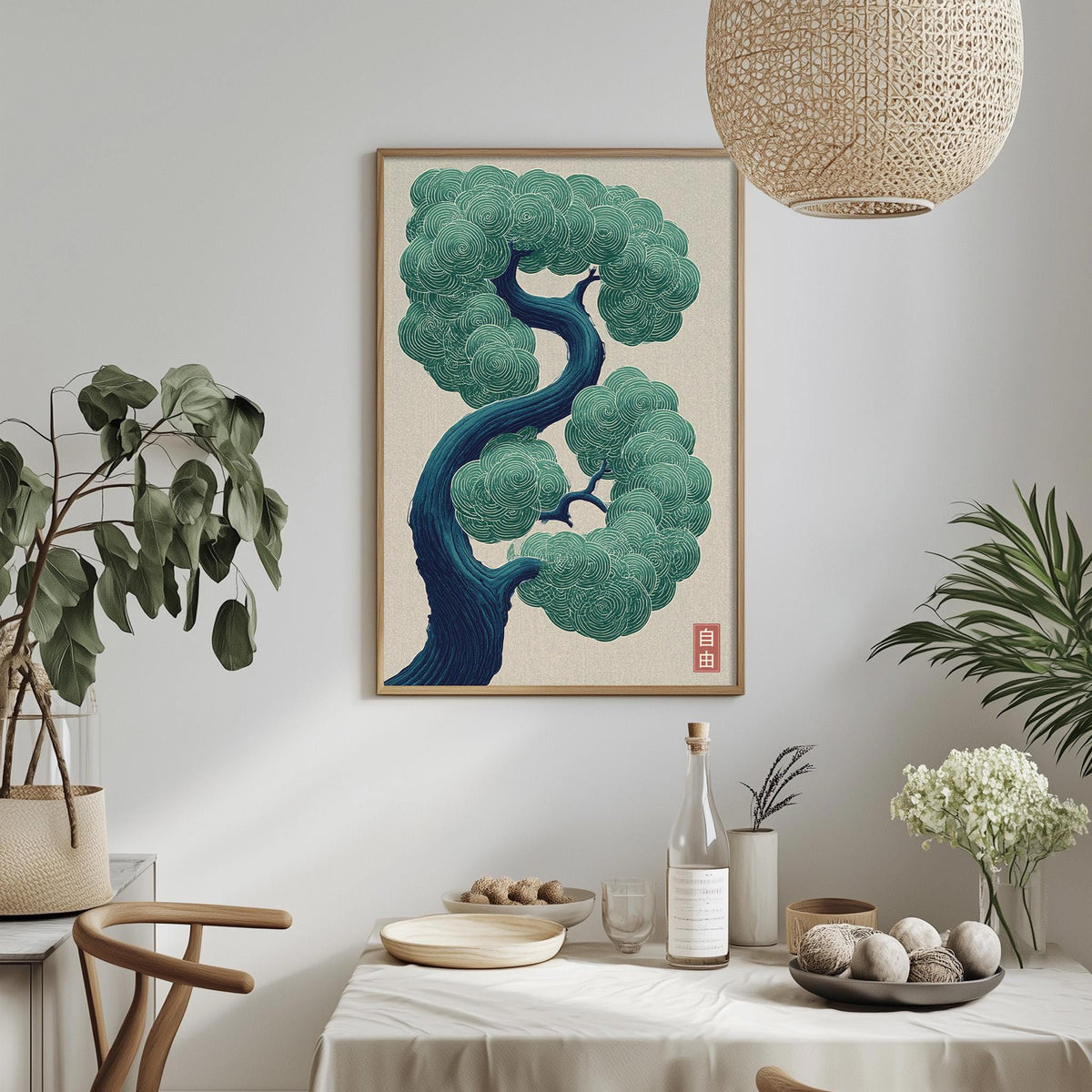 a dining table with a white tablecloth, a bowl of fruit, a bottle, and a vase with flowers. Above the table, there is a framed illustration of a tree with a blue trunk and green leaves. The table is set with a plate, a wine glass, and a small bowl. The room has a minimalist and modern design, with a hanging light fixture and potted plants adding to the decor.