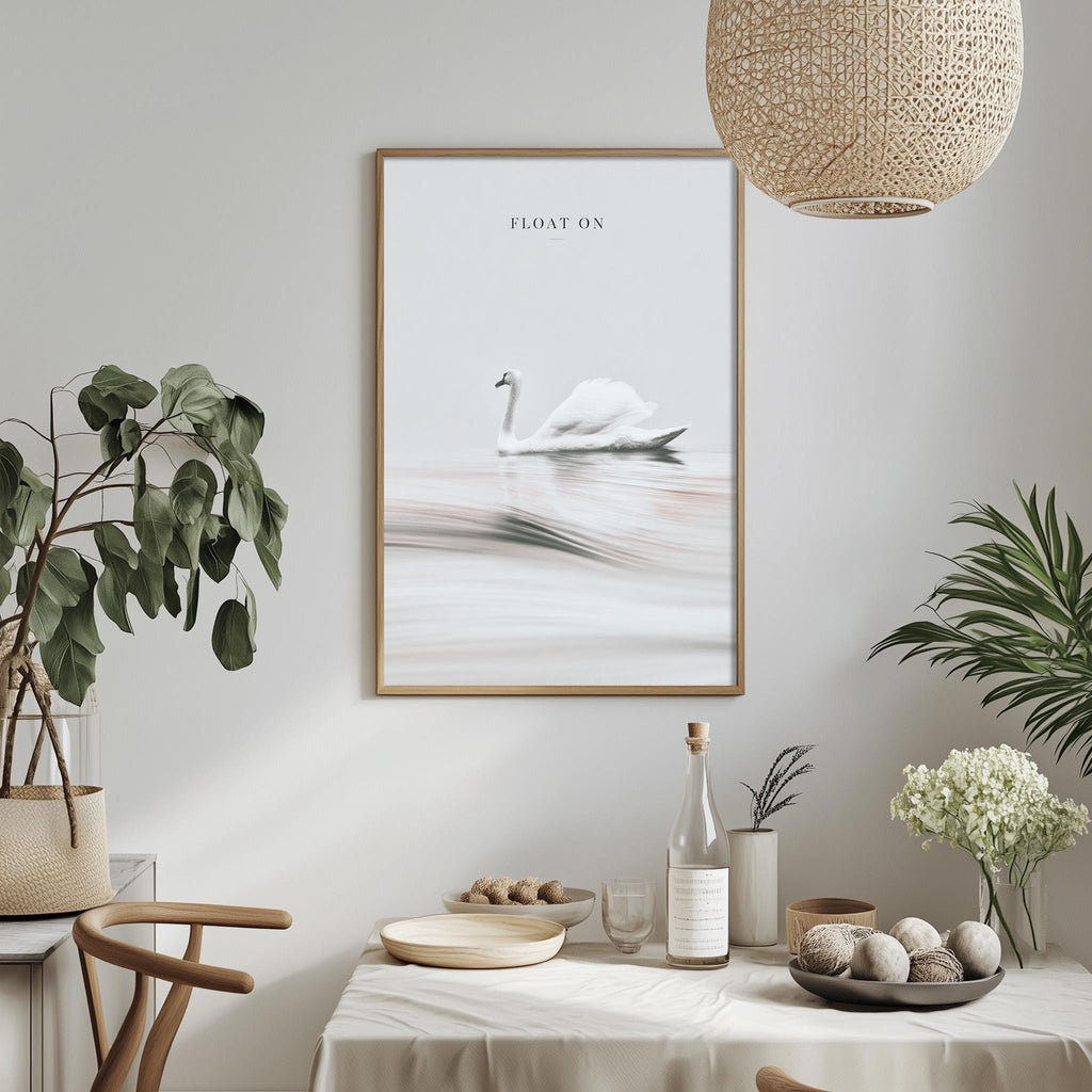 a dining table with a white tablecloth, a bowl of fruit, a bottle, and a vase with flowers. Above the table, there is a framed picture of a swan floating on a lake.