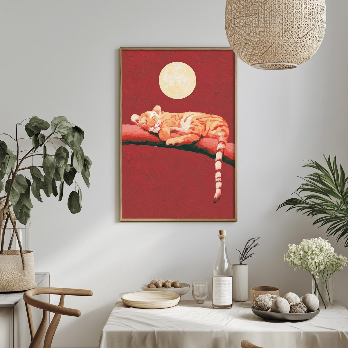 a dining table with a white tablecloth, a bowl of fruit, a bottle, and a vase with flowers. Above the table, there is a framed painting of a tiger resting on a branch, with a large moon in the background.